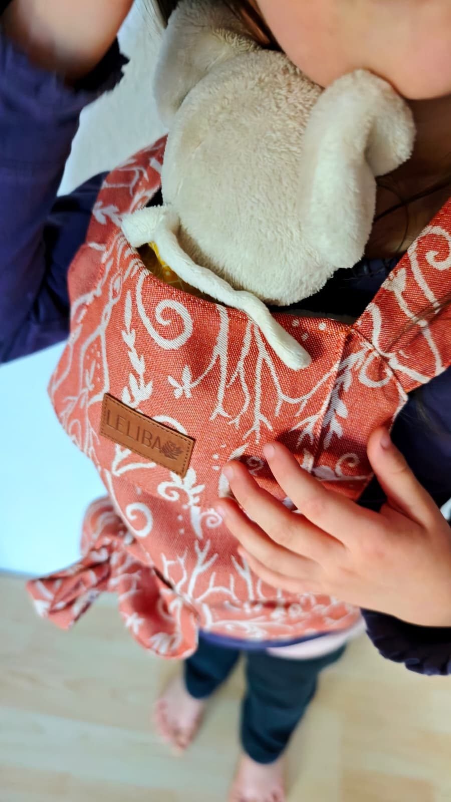 Kind trägt sein Kuscheltier in einer eigenen kleinen Puppentragehilfe